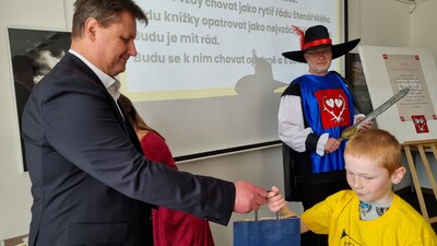 Pan starosta Milan Slavík předává  pasovanému malému čtenáři taštičku s drobnými dárky